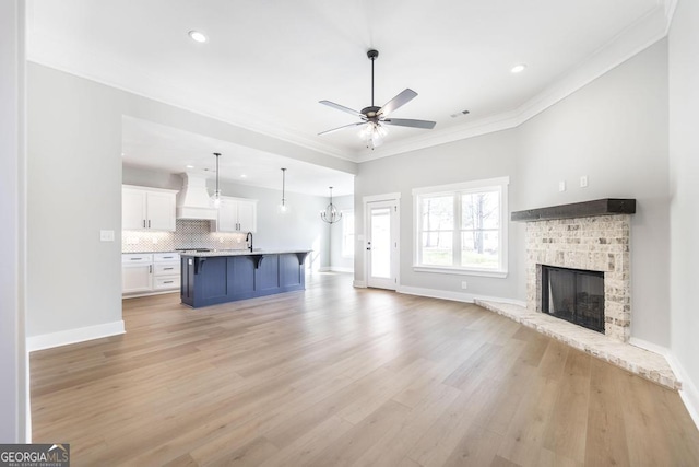 unfurnished living room with sink, crown molding, a fireplace, and light hardwood / wood-style floors