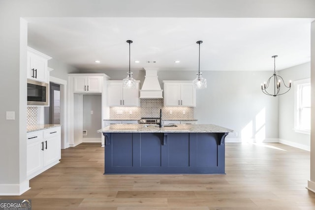 kitchen with a center island with sink, light stone countertops, custom range hood, and white cabinets