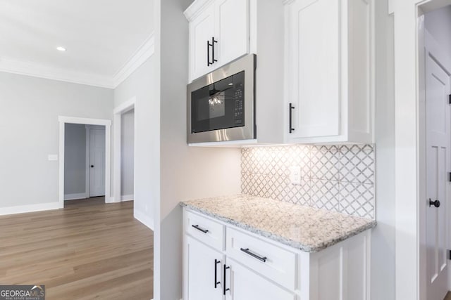 kitchen featuring stainless steel microwave, white cabinets, backsplash, ornamental molding, and light stone countertops