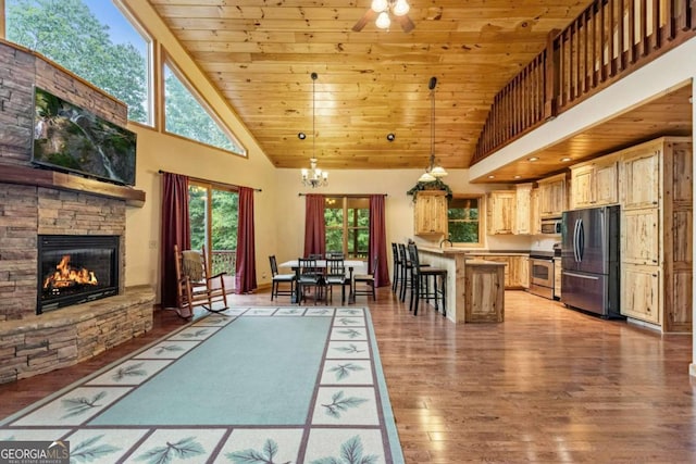 living room with light wood-type flooring, ceiling fan with notable chandelier, high vaulted ceiling, wooden ceiling, and a fireplace