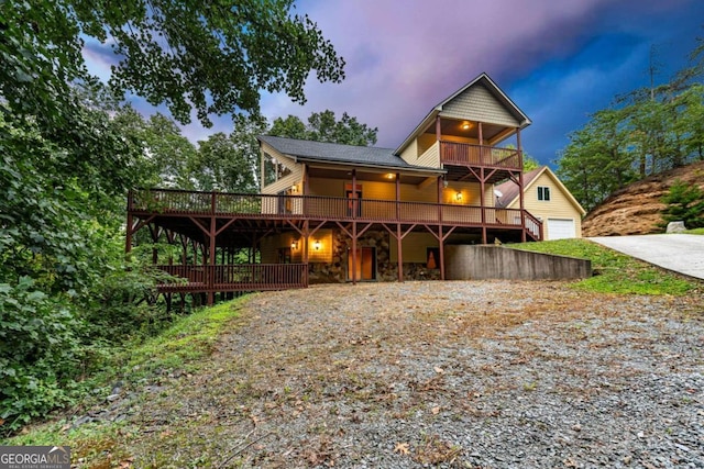 back house at dusk with a balcony, a deck, and a garage