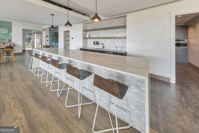 bar with tasteful backsplash, oven, light stone countertops, hanging light fixtures, and dark hardwood / wood-style floors