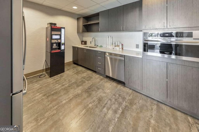 kitchen with light wood-type flooring, appliances with stainless steel finishes, sink, dark brown cabinets, and a drop ceiling