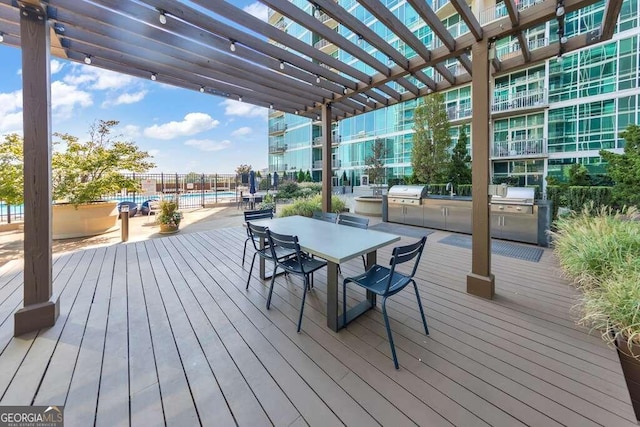 wooden terrace with exterior kitchen, a pergola, a swimming pool, and grilling area