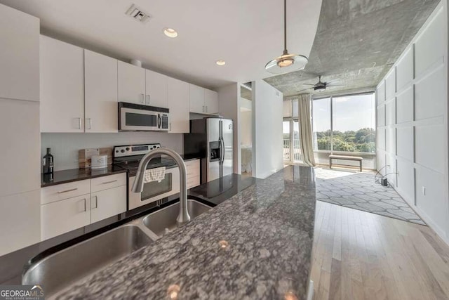 kitchen with appliances with stainless steel finishes, light hardwood / wood-style floors, white cabinetry, ceiling fan, and dark stone counters