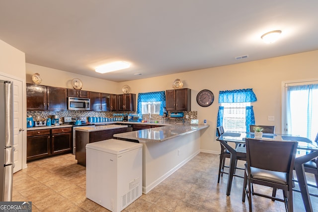 kitchen featuring dark brown cabinets, appliances with stainless steel finishes, kitchen peninsula, and a breakfast bar