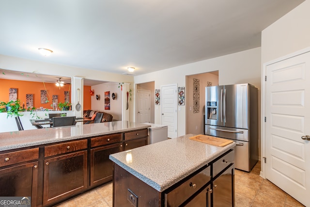 kitchen with stainless steel fridge, light tile patterned flooring, a center island, ceiling fan, and dark brown cabinetry