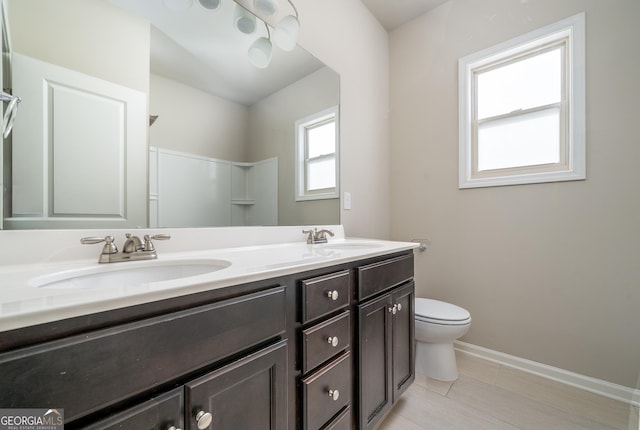 full bathroom with baseboards, double vanity, a sink, and toilet