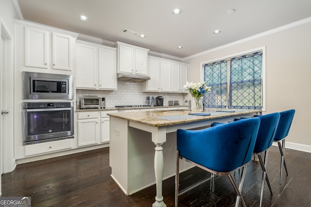 kitchen featuring appliances with stainless steel finishes, white cabinetry, dark wood-type flooring, an island with sink, and backsplash