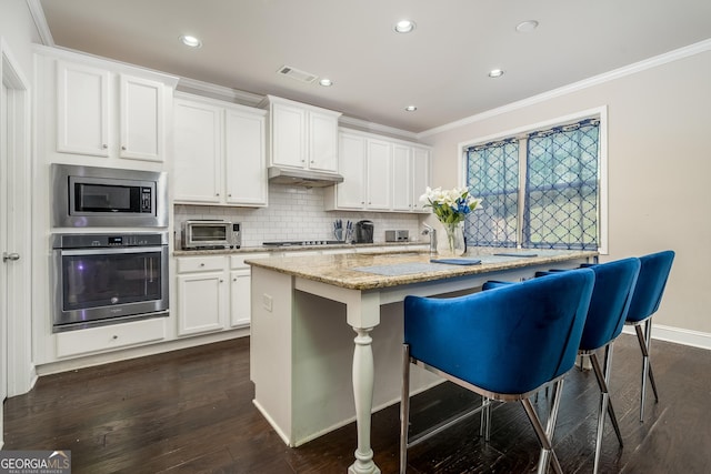 kitchen with white cabinets, stainless steel appliances, a center island with sink, a kitchen breakfast bar, and light stone countertops