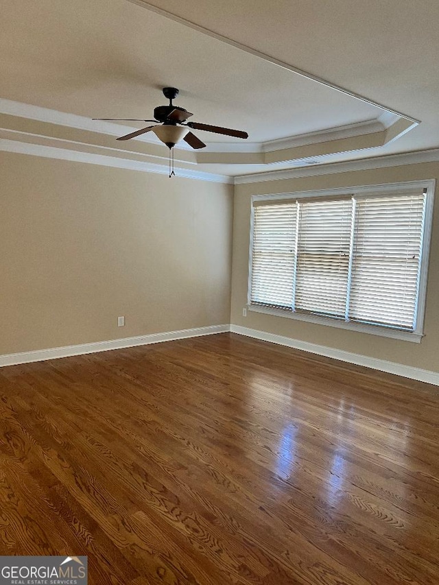 unfurnished room featuring ceiling fan, a raised ceiling, ornamental molding, and dark wood-type flooring