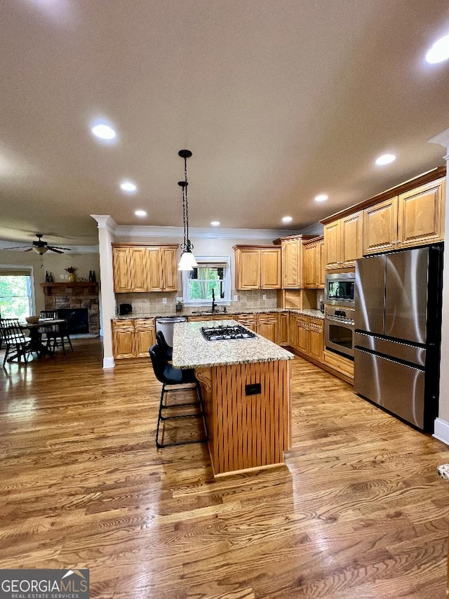 kitchen with tasteful backsplash, light stone counters, stainless steel appliances, a kitchen island, and hanging light fixtures