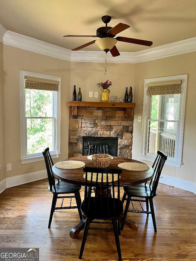 dining space with hardwood / wood-style flooring, ceiling fan, ornamental molding, and a fireplace