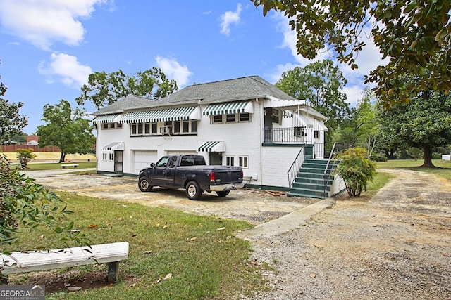 view of front of house featuring an attached garage, dirt driveway, and stairway