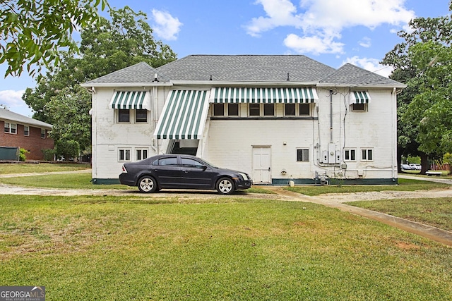 rear view of property featuring a shingled roof and a lawn