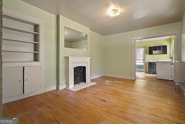 unfurnished living room featuring light wood-style floors, a brick fireplace, baseboards, and built in shelves