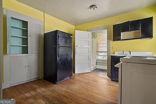 kitchen with light countertops, freestanding refrigerator, dark cabinets, range, and hardwood / wood-style flooring