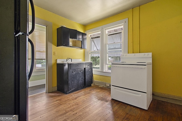 kitchen featuring white electric stove, baseboards, hardwood / wood-style flooring, dark cabinets, and freestanding refrigerator