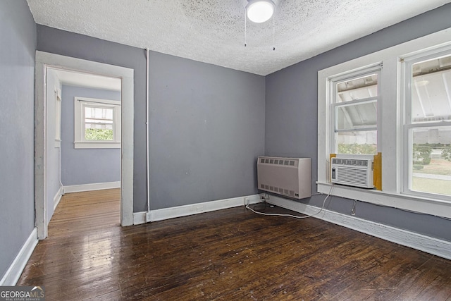 empty room featuring baseboards, wood-type flooring, heating unit, a textured ceiling, and cooling unit