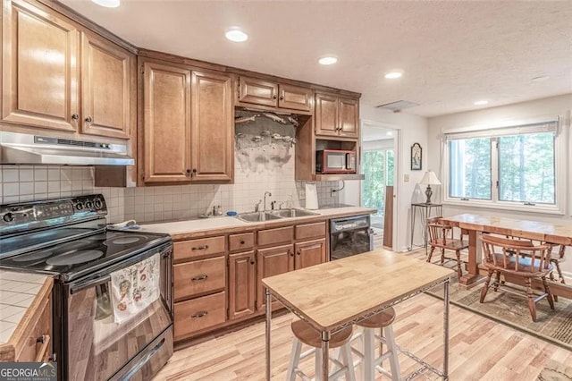 kitchen with sink, tile countertops, light hardwood / wood-style floors, and black appliances