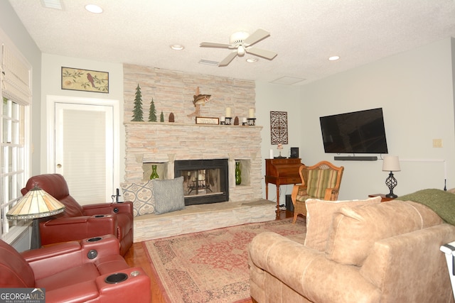 living room featuring ceiling fan, a stone fireplace, a textured ceiling, and hardwood / wood-style flooring