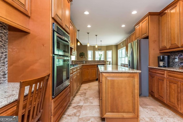 kitchen featuring light stone countertops, backsplash, appliances with stainless steel finishes, a center island, and kitchen peninsula