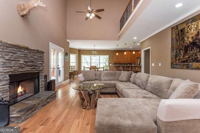 living room featuring crown molding, french doors, light wood-type flooring, a stone fireplace, and ceiling fan