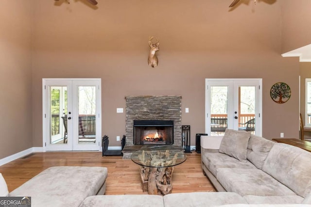 living room featuring light wood-type flooring, french doors, ceiling fan, and a stone fireplace