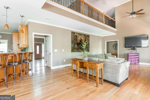 living room featuring crown molding, a towering ceiling, light hardwood / wood-style flooring, and ceiling fan