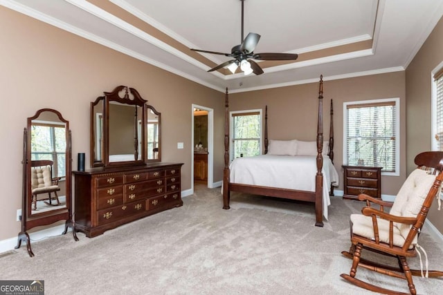 carpeted bedroom featuring multiple windows, ceiling fan, a tray ceiling, and ensuite bath