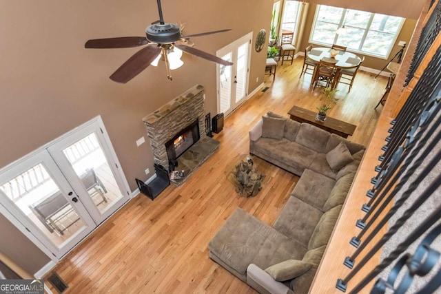 living room featuring light wood-type flooring, a high ceiling, ceiling fan, and a stone fireplace