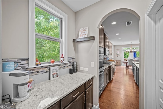 kitchen with hanging light fixtures, hardwood / wood-style floors, light stone countertops, dark brown cabinetry, and tasteful backsplash