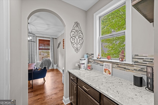 kitchen with backsplash, light stone counters, a chandelier, wood-type flooring, and dark brown cabinetry