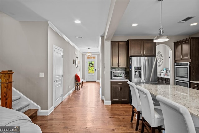 kitchen with decorative light fixtures, appliances with stainless steel finishes, light stone counters, wood-type flooring, and ornamental molding