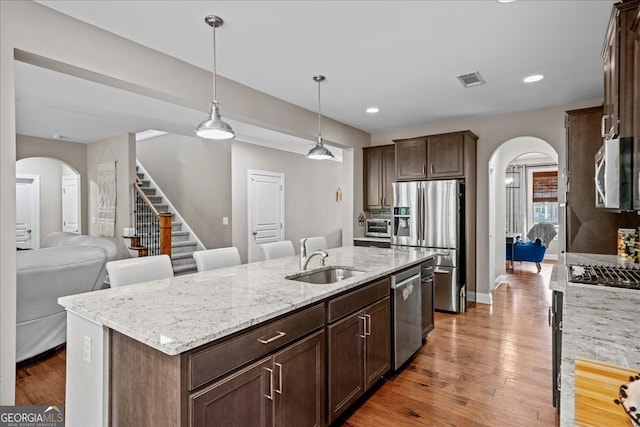 kitchen with hardwood / wood-style floors, appliances with stainless steel finishes, a kitchen island with sink, sink, and light stone counters