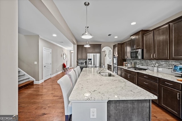 kitchen with hanging light fixtures, appliances with stainless steel finishes, light stone counters, dark hardwood / wood-style floors, and an island with sink