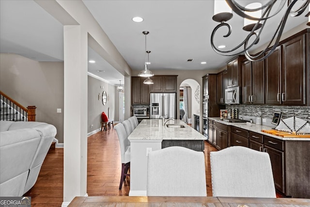 kitchen with decorative light fixtures, stainless steel appliances, an island with sink, dark wood-type flooring, and a kitchen breakfast bar