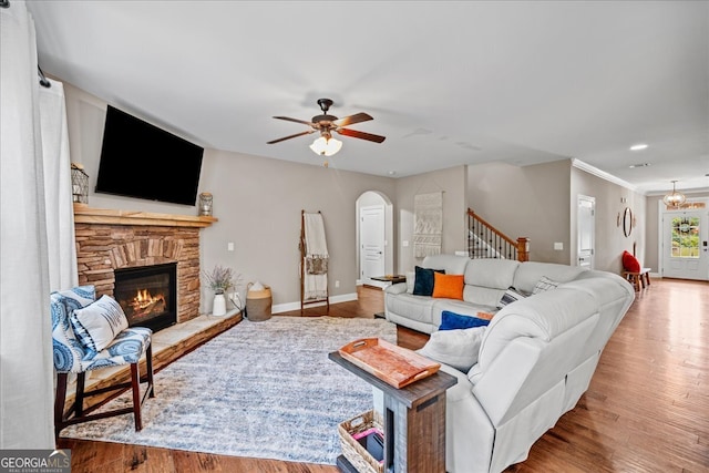 living room featuring crown molding, ceiling fan with notable chandelier, hardwood / wood-style flooring, and a fireplace