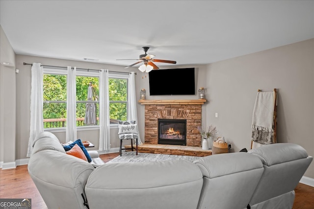 living room featuring ceiling fan, a stone fireplace, and wood-type flooring