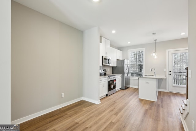 kitchen featuring stainless steel appliances, a sink, white cabinets, hanging light fixtures, and an island with sink