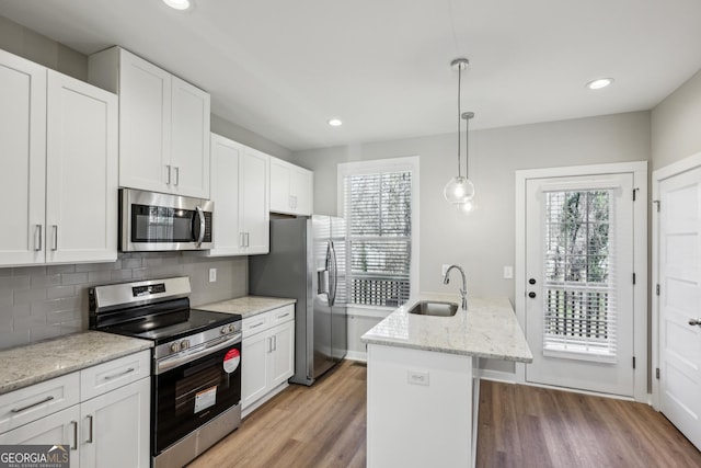 kitchen featuring stainless steel appliances, a sink, white cabinets, an island with sink, and pendant lighting