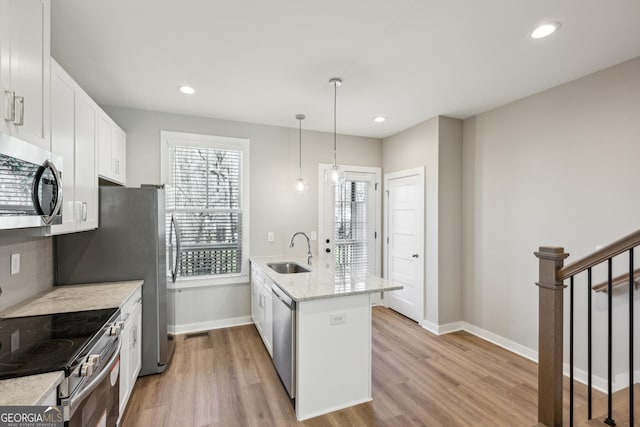 kitchen featuring light stone counters, hanging light fixtures, appliances with stainless steel finishes, white cabinetry, and a sink