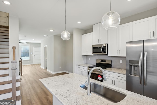 kitchen featuring hanging light fixtures, white cabinetry, stainless steel appliances, and a sink