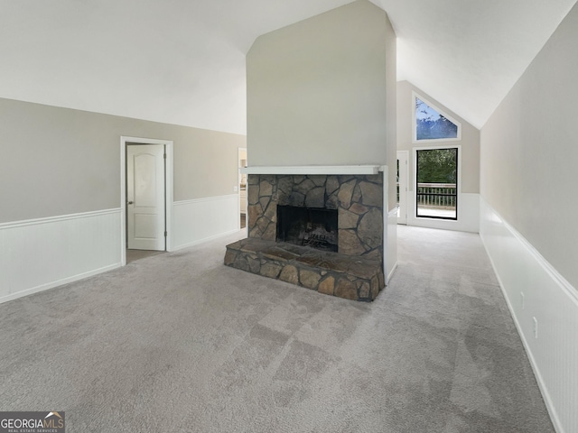 unfurnished living room with a wainscoted wall, a stone fireplace, carpet, and high vaulted ceiling