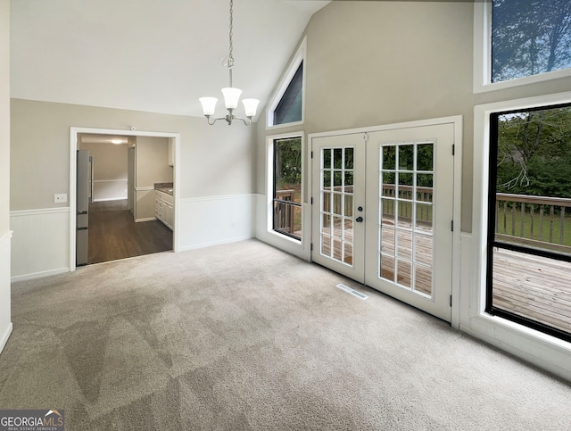 unfurnished dining area featuring carpet flooring, a notable chandelier, high vaulted ceiling, and french doors