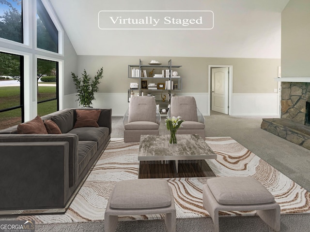 living area with light carpet, high vaulted ceiling, a stone fireplace, and wainscoting