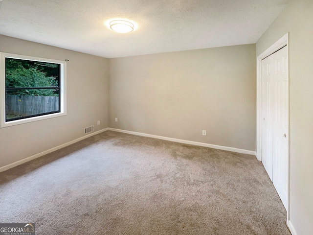 unfurnished bedroom featuring a textured ceiling, light colored carpet, and a closet