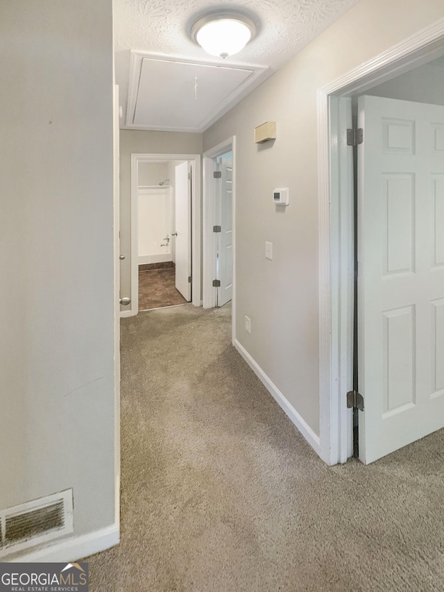 hallway featuring a textured ceiling, attic access, baseboards, and carpet floors