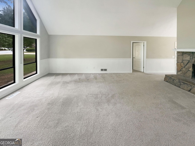 unfurnished living room with visible vents, a wainscoted wall, carpet floors, high vaulted ceiling, and a stone fireplace