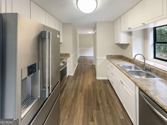 kitchen featuring dark wood finished floors, appliances with stainless steel finishes, white cabinets, a textured ceiling, and a sink
